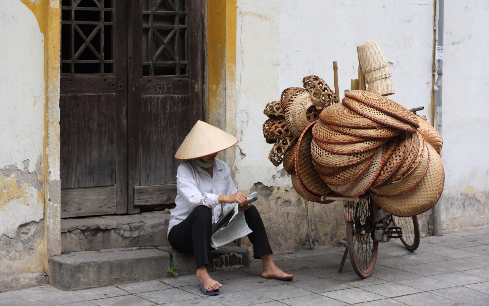 Người bán thúng ngồi bên xe đạp trên một phố cũ Hà Nội